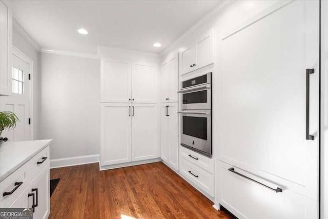 kitchen with ornamental molding, white cabinetry, dark wood-type flooring, and stainless steel double oven