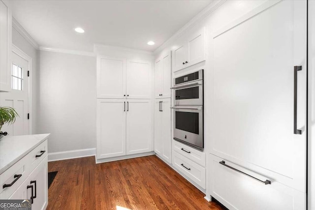 kitchen with dark wood finished floors, crown molding, double oven, light countertops, and white cabinets
