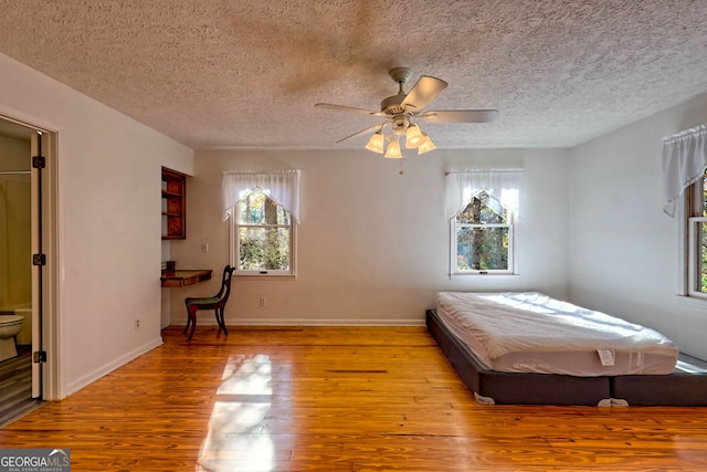 bedroom featuring light hardwood / wood-style floors, a textured ceiling, ensuite bath, and ceiling fan