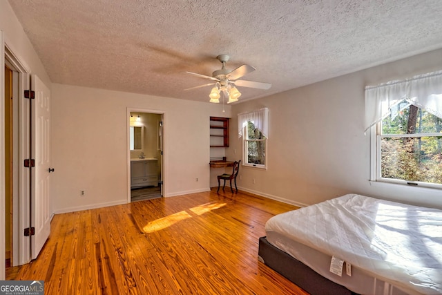 unfurnished bedroom with built in desk, ceiling fan, a textured ceiling, connected bathroom, and light wood-type flooring