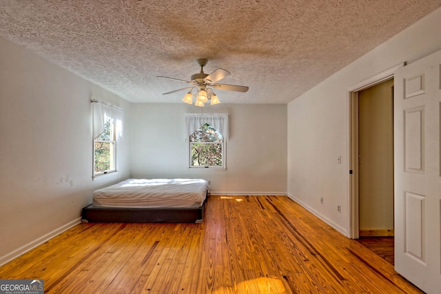 unfurnished bedroom featuring multiple windows, a textured ceiling, wood-type flooring, and ceiling fan