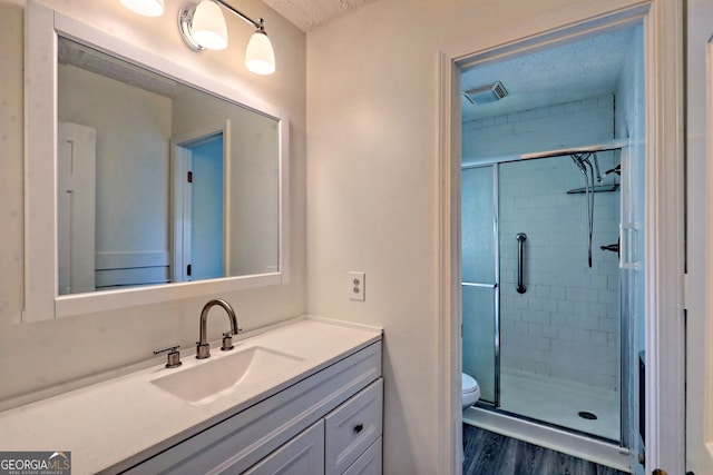 bathroom with a shower with door, wood-type flooring, a textured ceiling, toilet, and vanity