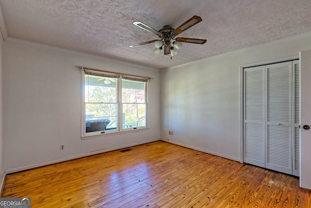 unfurnished bedroom with a closet, crown molding, light wood-type flooring, a textured ceiling, and ceiling fan