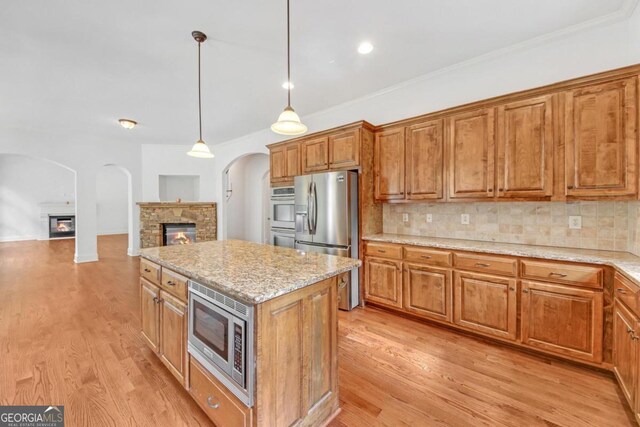 kitchen with a center island, a fireplace, appliances with stainless steel finishes, tasteful backsplash, and decorative light fixtures