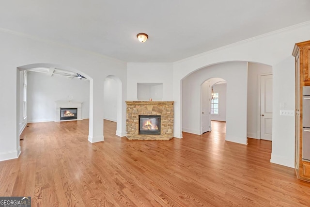 unfurnished living room with a stone fireplace, ceiling fan, light hardwood / wood-style floors, and ornamental molding