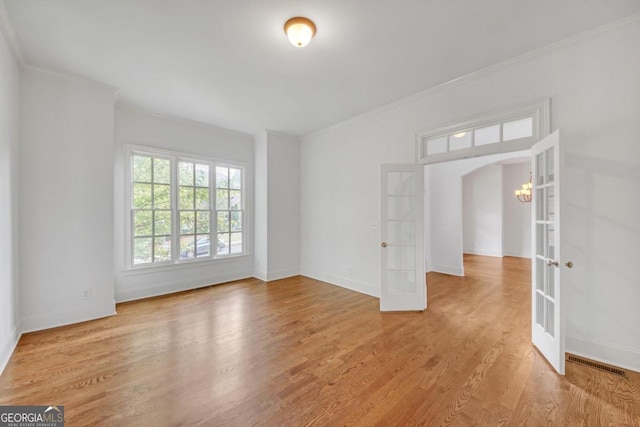 empty room featuring hardwood / wood-style flooring, a notable chandelier, ornamental molding, and french doors