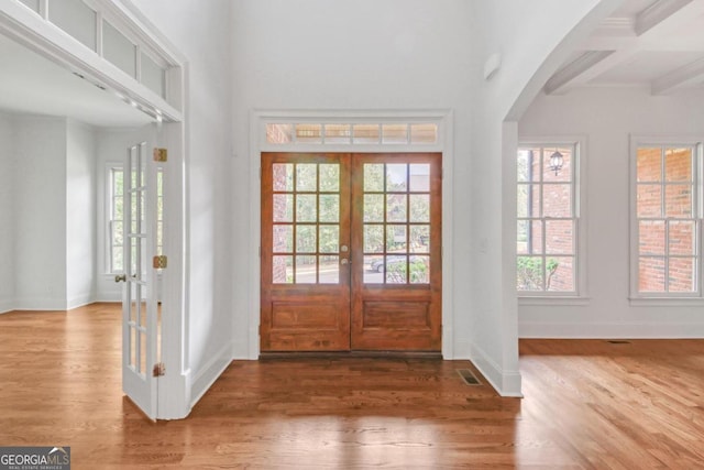 entrance foyer featuring beamed ceiling, plenty of natural light, wood-type flooring, and french doors