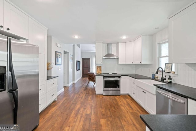 kitchen with stainless steel appliances, dark wood-type flooring, wall chimney exhaust hood, white cabinets, and sink