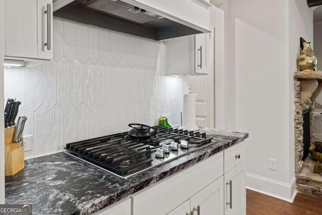 kitchen with dark stone counters, white cabinets, stainless steel gas stovetop, exhaust hood, and dark hardwood / wood-style floors