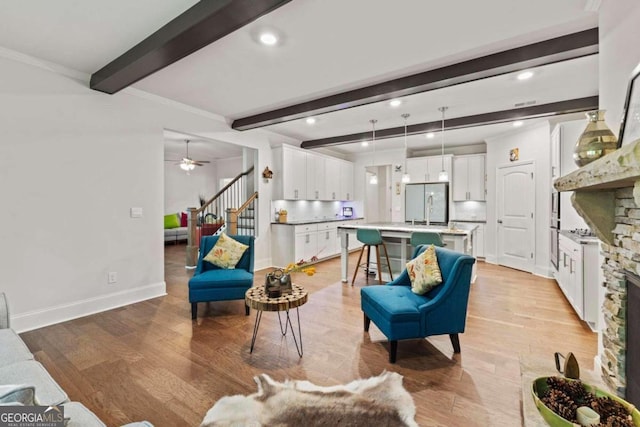 living room featuring crown molding, a stone fireplace, ceiling fan, light hardwood / wood-style floors, and beam ceiling