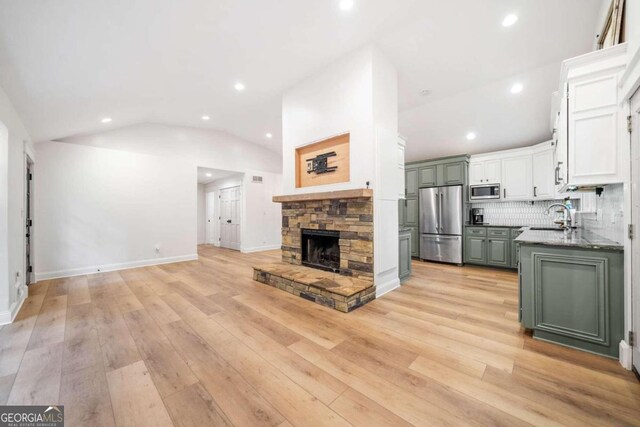 interior space with lofted ceiling, white cabinets, a stone fireplace, light hardwood / wood-style flooring, and appliances with stainless steel finishes