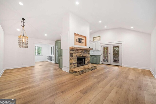 unfurnished living room featuring french doors, lofted ceiling, a fireplace, and light hardwood / wood-style flooring