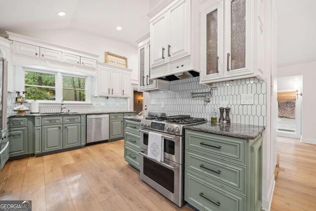 kitchen with decorative backsplash, appliances with stainless steel finishes, white cabinets, light hardwood / wood-style floors, and lofted ceiling