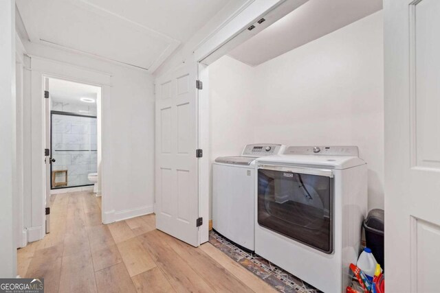 clothes washing area with washer and clothes dryer and light wood-type flooring