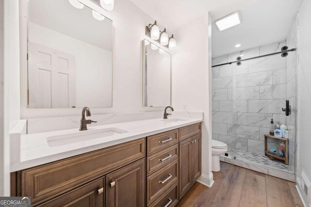 bathroom with hardwood / wood-style flooring, vanity, toilet, and tiled shower