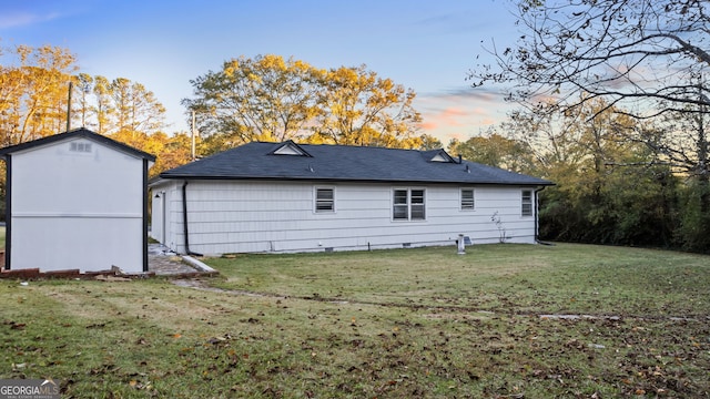 back house at dusk with a lawn and a storage unit