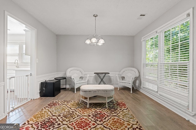 living area with an inviting chandelier, a textured ceiling, and light wood-type flooring