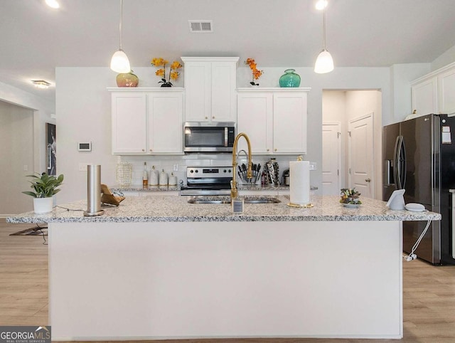 kitchen featuring pendant lighting, white cabinets, an island with sink, appliances with stainless steel finishes, and light hardwood / wood-style floors