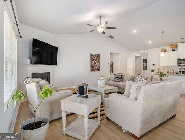 living room featuring ceiling fan, light hardwood / wood-style flooring, and vaulted ceiling