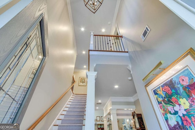 stairway featuring a towering ceiling, ornamental molding, and ornate columns