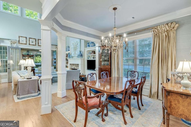 dining area with a high ceiling, crown molding, decorative columns, light wood-type flooring, and a chandelier