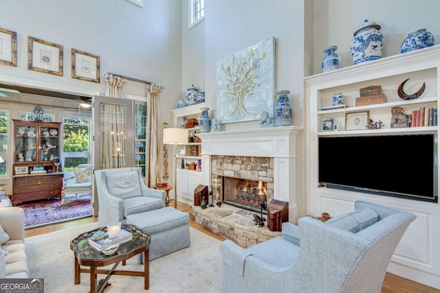 living room featuring a towering ceiling, a stone fireplace, and light wood-type flooring