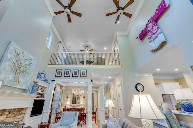 living room with a stone fireplace, ornamental molding, a high ceiling, and an inviting chandelier