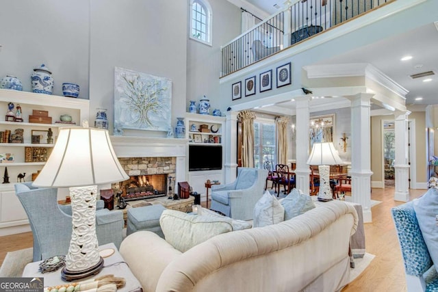 living room with a stone fireplace, ornate columns, a towering ceiling, and plenty of natural light