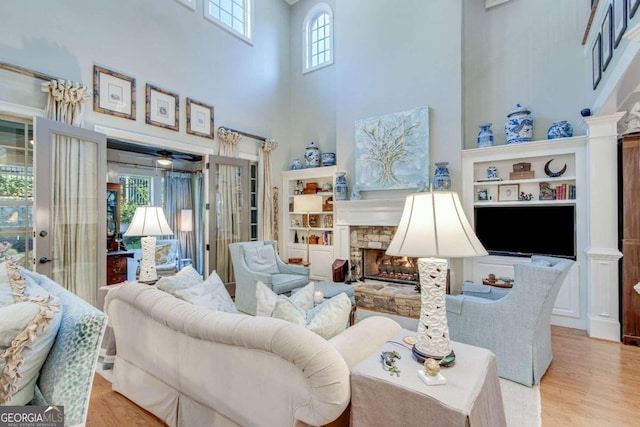 living room featuring a stone fireplace, light wood-type flooring, and a towering ceiling