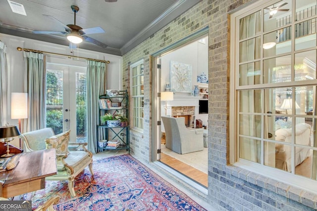 sitting room featuring a stone fireplace, ornamental molding, hardwood / wood-style flooring, and ceiling fan