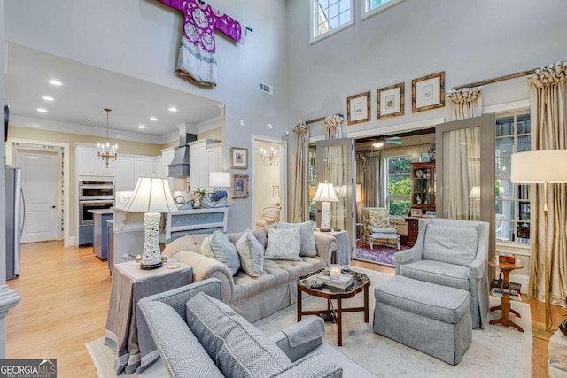 living room featuring a towering ceiling, crown molding, light hardwood / wood-style flooring, and a healthy amount of sunlight