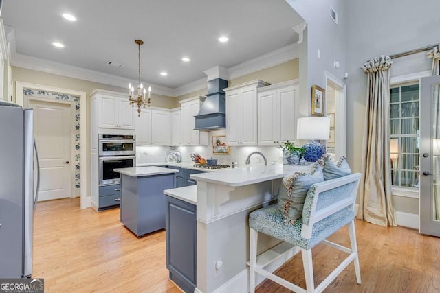 kitchen featuring custom exhaust hood, a breakfast bar area, stainless steel appliances, decorative light fixtures, and a center island