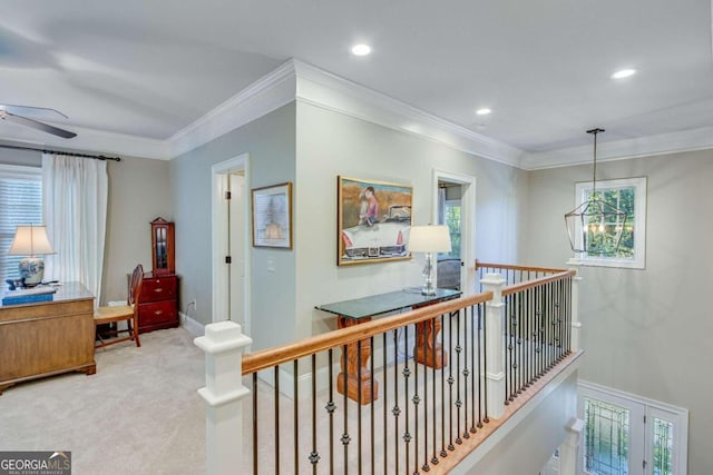 hall with ornamental molding, an inviting chandelier, plenty of natural light, and light colored carpet