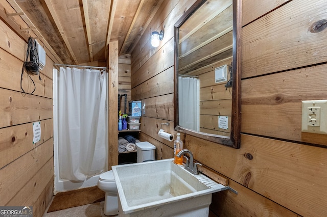 bathroom featuring sink, a shower with shower curtain, toilet, and wood walls