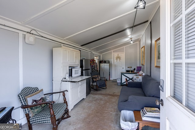 interior space featuring stainless steel refrigerator, lofted ceiling, and white cabinets