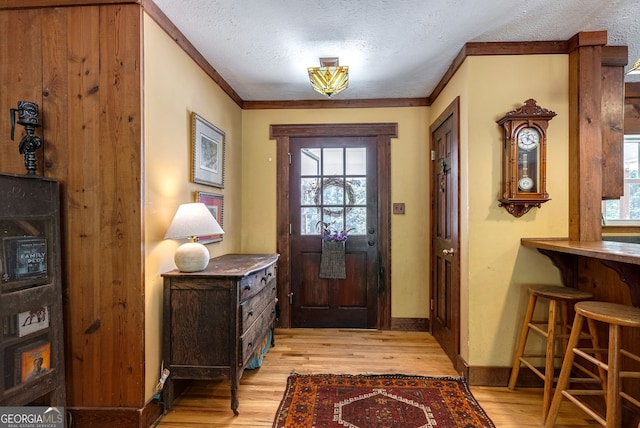 doorway to outside with a textured ceiling, light hardwood / wood-style flooring, and ornamental molding