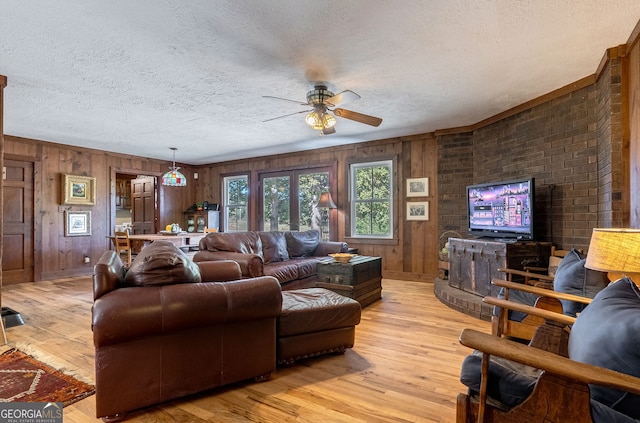 living room featuring a textured ceiling, wooden walls, light wood-type flooring, and ceiling fan