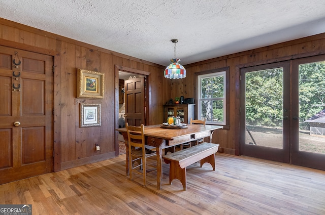 dining area with french doors, wood walls, and light wood-type flooring