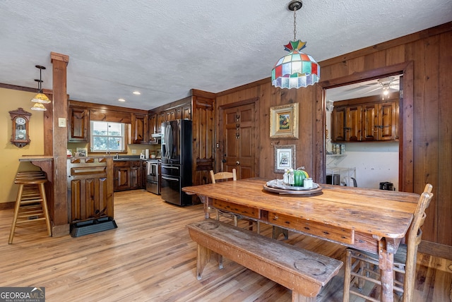 dining area with wood walls, ornamental molding, a textured ceiling, and light wood-type flooring