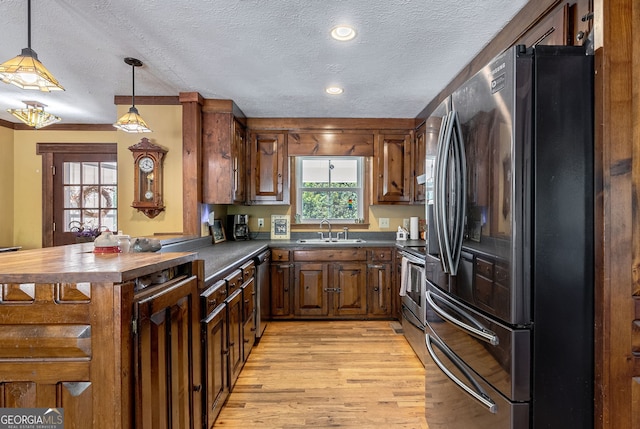 kitchen featuring appliances with stainless steel finishes, sink, a textured ceiling, light hardwood / wood-style floors, and pendant lighting