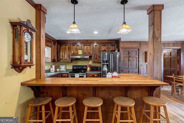 kitchen featuring exhaust hood, light hardwood / wood-style flooring, appliances with stainless steel finishes, a textured ceiling, and wood walls