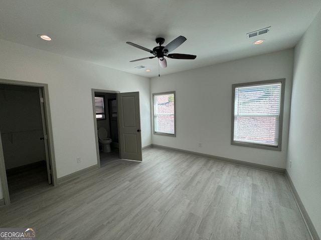 unfurnished bedroom with light hardwood / wood-style floors, multiple windows, a spacious closet, and ensuite bathroom