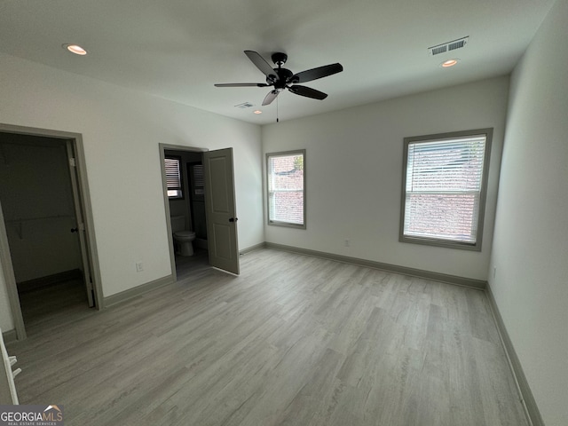 unfurnished bedroom featuring ceiling fan, ensuite bathroom, a closet, light hardwood / wood-style floors, and a walk in closet