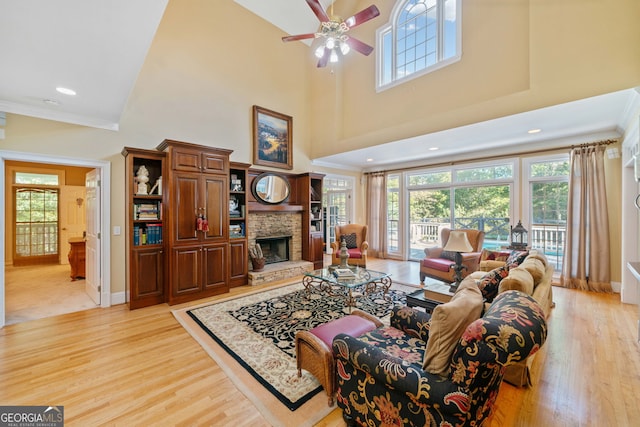 living room with a stone fireplace, light hardwood / wood-style flooring, crown molding, and a towering ceiling