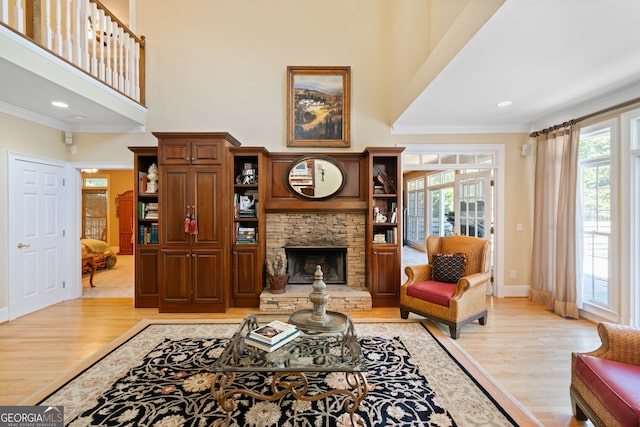 living room with light hardwood / wood-style floors, crown molding, a stone fireplace, and a towering ceiling