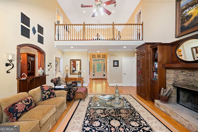 living room with light hardwood / wood-style floors, high vaulted ceiling, crown molding, and a stone fireplace