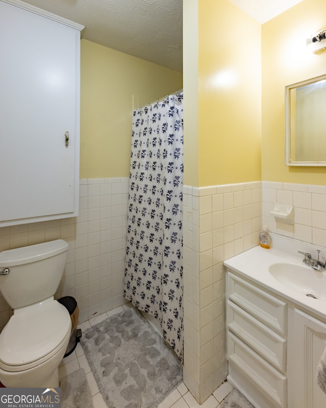 bathroom featuring a textured ceiling, tile walls, toilet, vanity, and tile patterned flooring