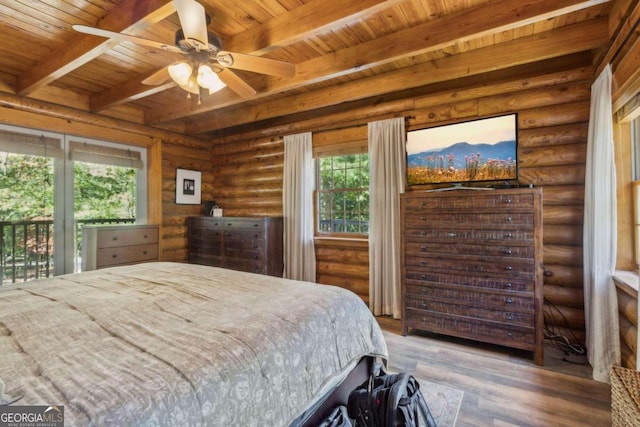 bedroom featuring log walls, multiple windows, wood-type flooring, and ceiling fan