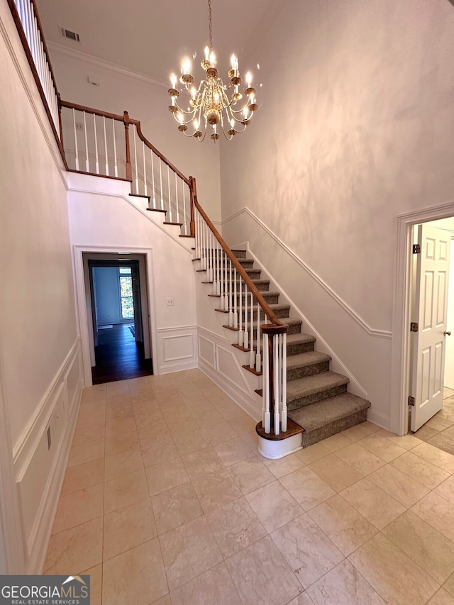 staircase featuring a notable chandelier, ornamental molding, and a high ceiling