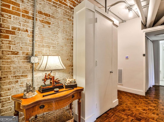 hall with dark parquet flooring and brick wall